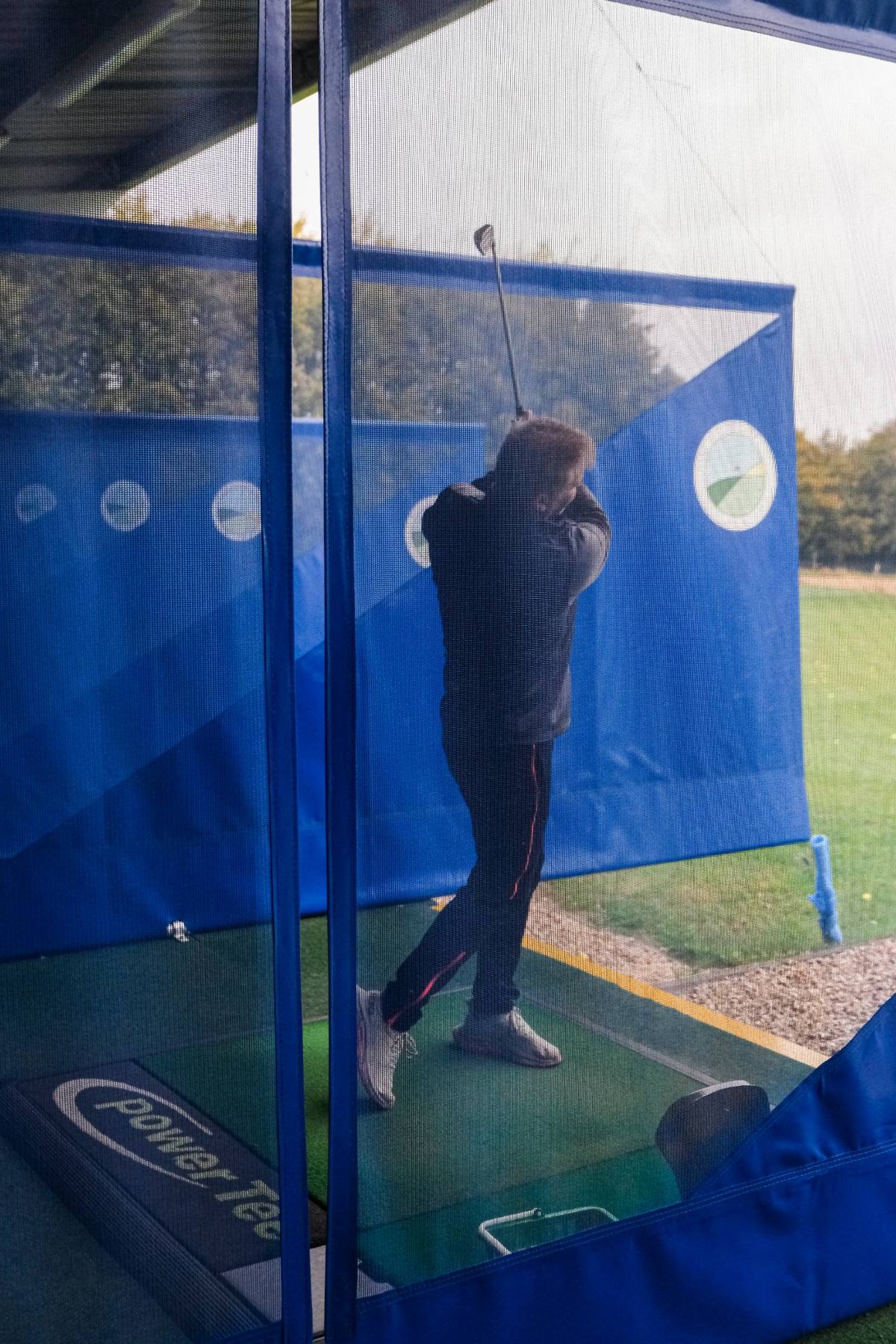 A golfer mid-swing in a covered bay at Winchester Golf Academy