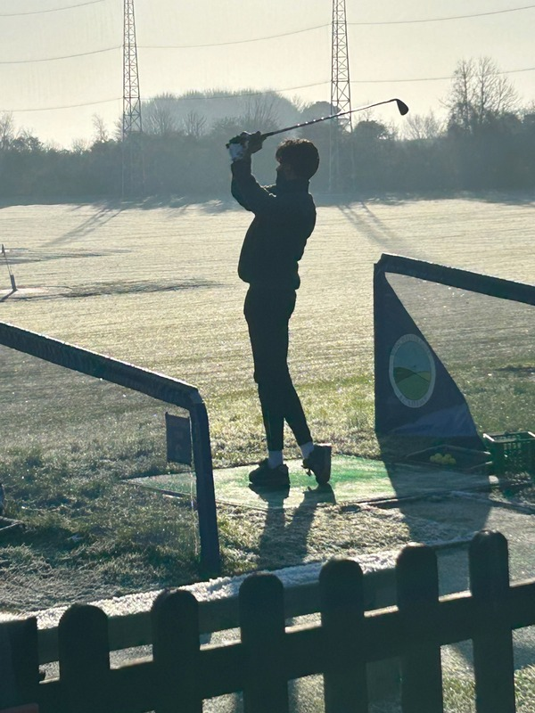Golfer mid-swing on a frosty sunrise morning at the range