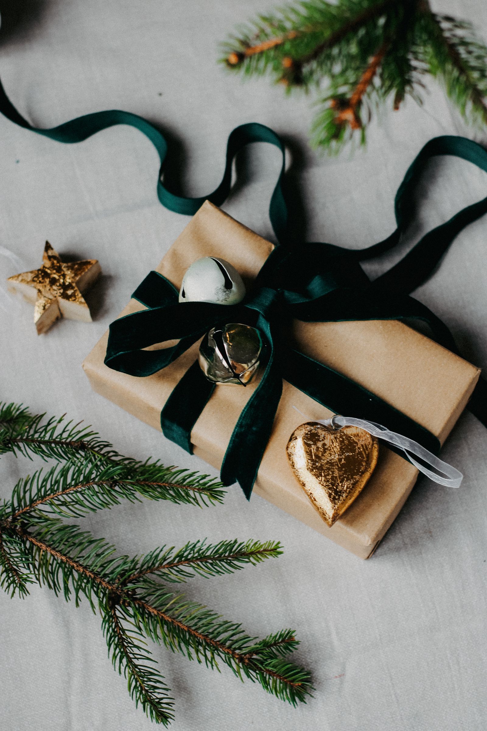 A wrapped Christmas gift with a green velvet ribbon, pine sprigs and a gold heart charm
